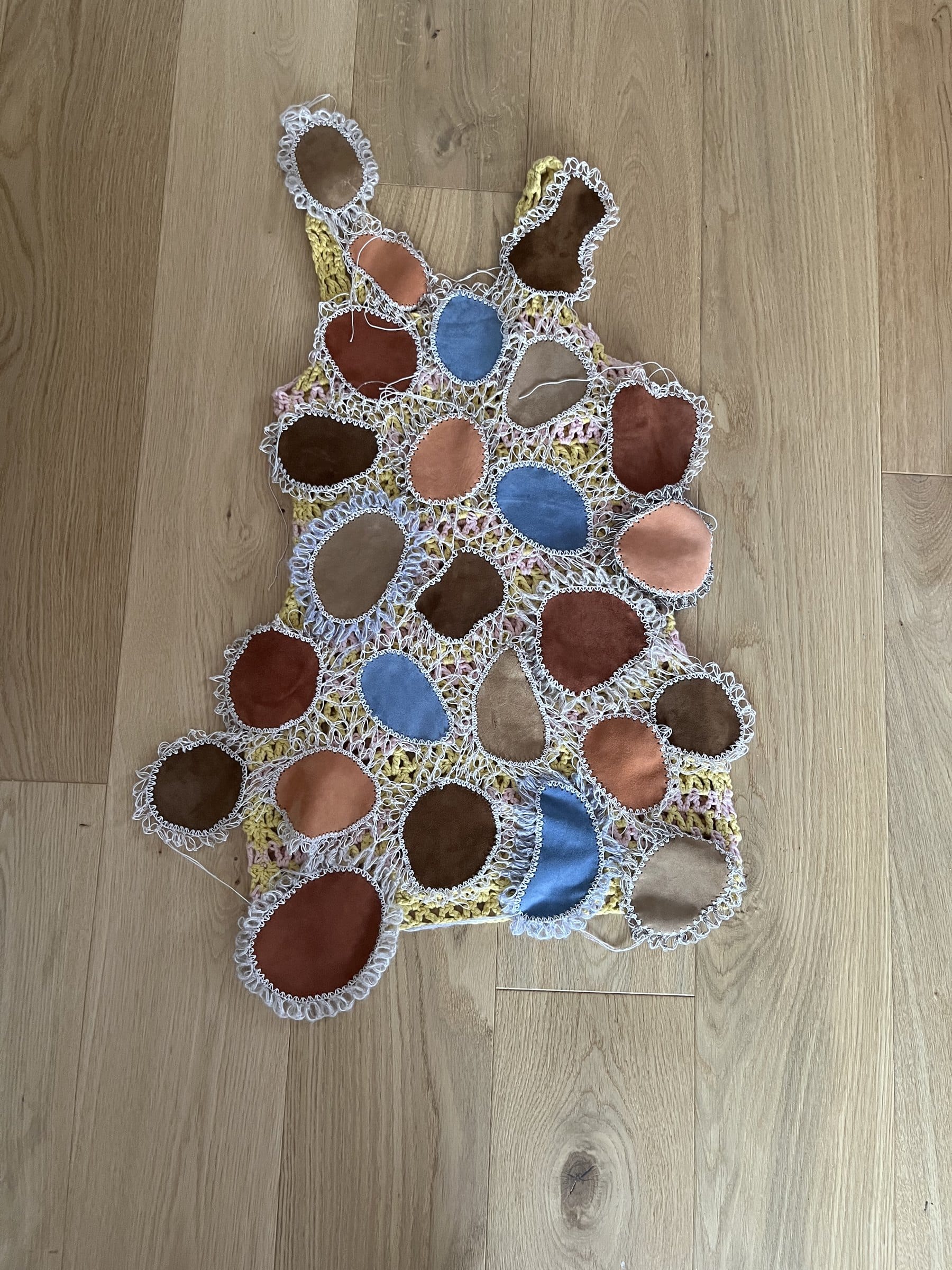 Erster Teil des Kleids, mit Häkelarbeit verbundene Lederpatches, auf Holzboden liegend